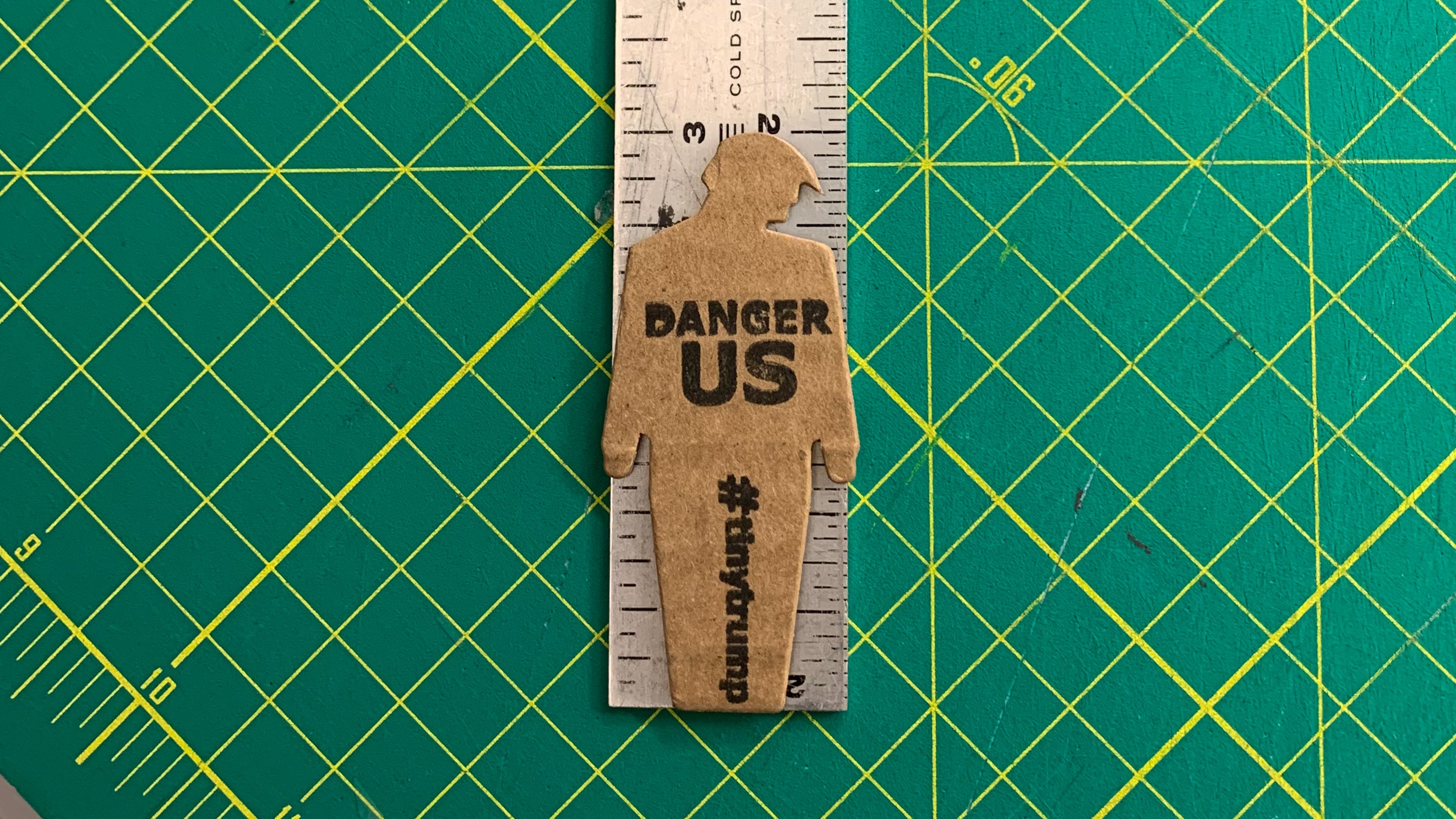 tiny trump with the slogan "Danger US" stuck to a ruler, indicating it is 3 inches tall