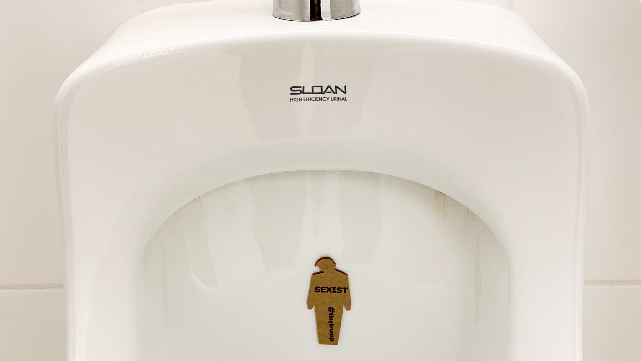 tiny trump with the slogan "Sexist" stuck to a urinal