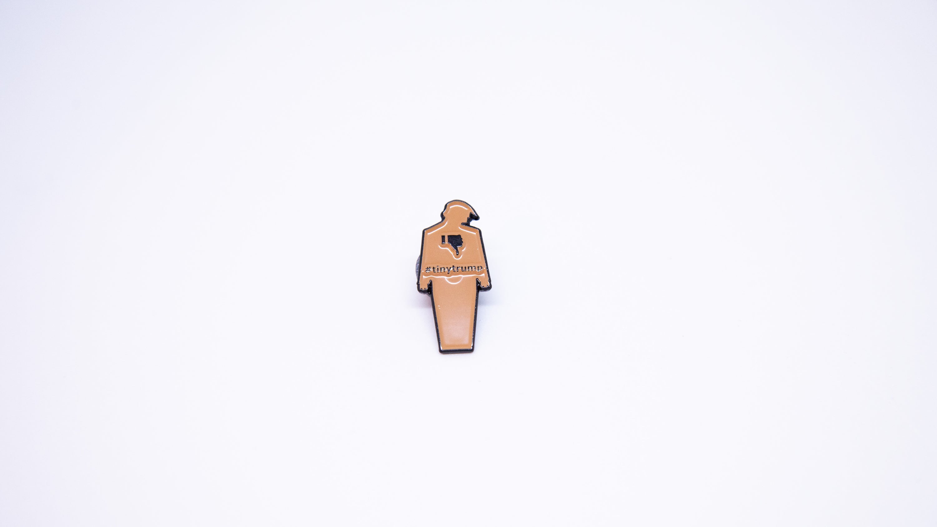 Close up shot of a 1.5" tiny trump enamel pin shown with a thumbs down sign