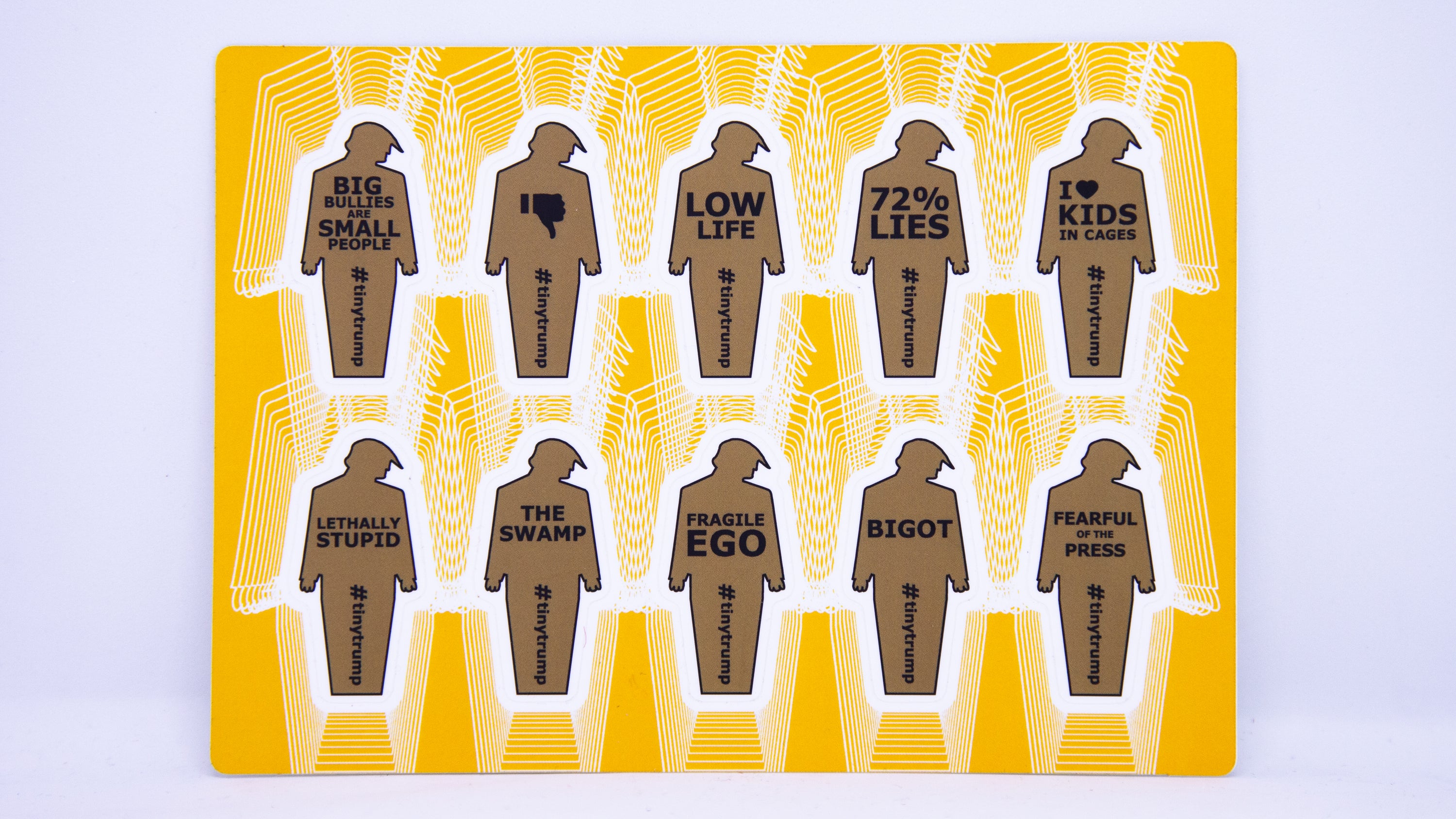 A sticker sheet with 10 two inch tall tiny trumps with the following slogans: Big Bullies Are Small People, thumbs down symbol, Low Life, 72% Lies, I heart Kids in Cages, Lethally Stupid, The Swamp, Fragile Ego, Bigot, Fearful of the Press