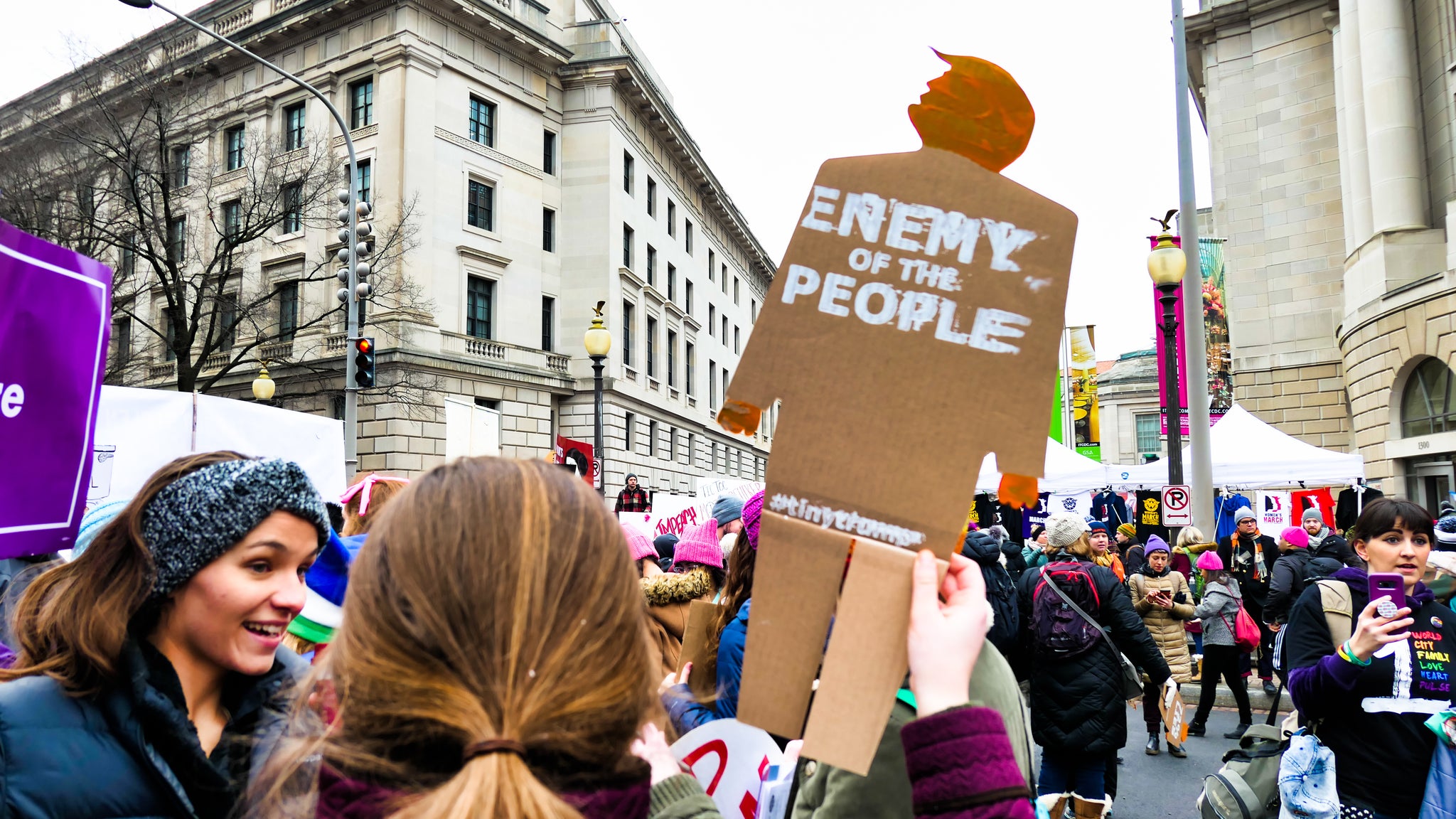 Protester at a march holding a 2 foot tall, cardboard tiny trump that has "Enemy of the People" stamped on it