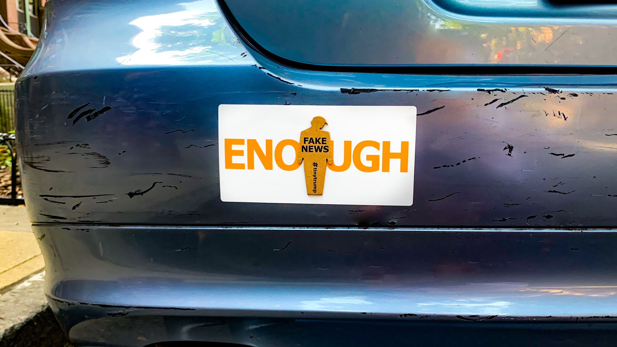 "ENOUGH" tiny trump bumper sticker shown with a "Fake News" tiny trump stuck on top