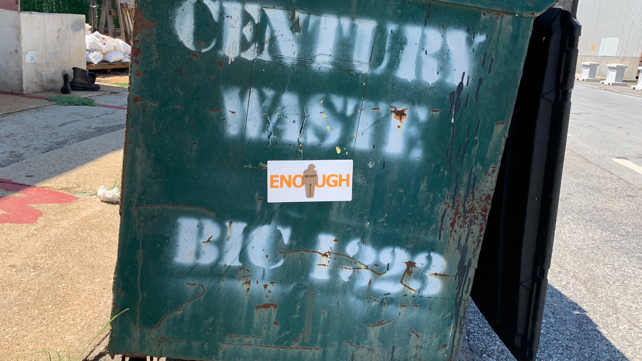 "ENOUGH" tiny trump sticker shown for scale, stuck in the middle of a green Century Waste dumpster