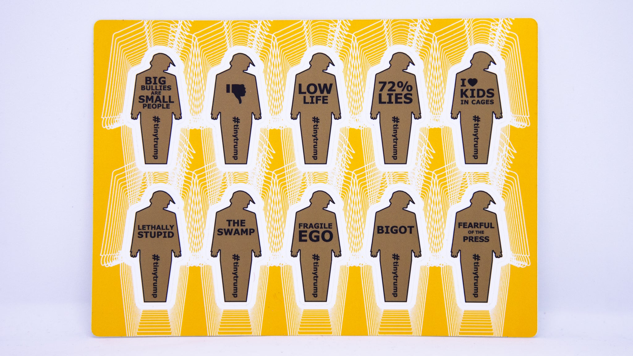 A sticker sheet with 10 two inch tall tiny trumps with the following slogans: Big Bullies Are Small People, thumbs down symbol, Low Life, 72% Lies, I heart Kids in Cages, Lethally Stupid, The Swamp, Fragile Ego, Bigot, Fearful of the Press